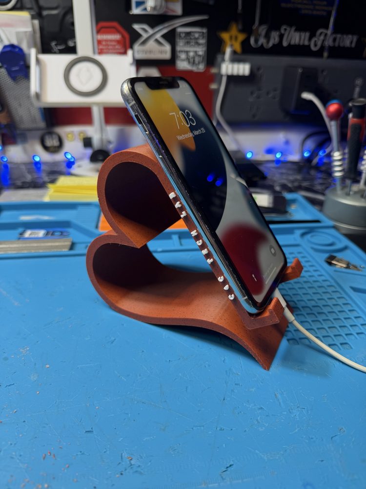iPhone resting on the heart-shaped 3D-printed stand while charging