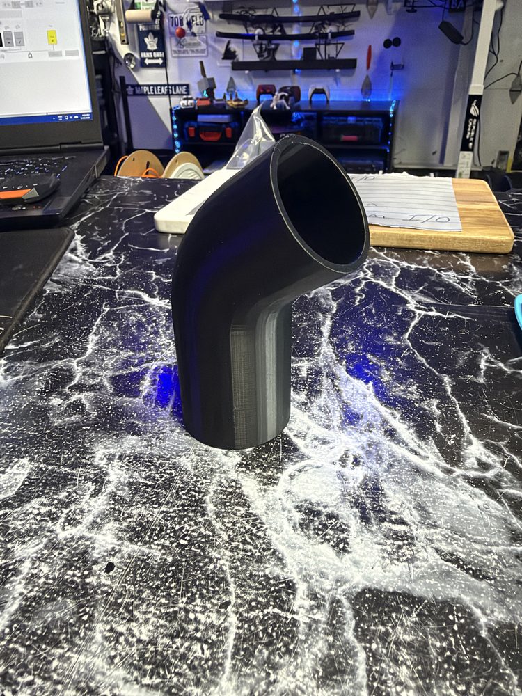 Black 3D-printed bent pipe fitting on a workbench